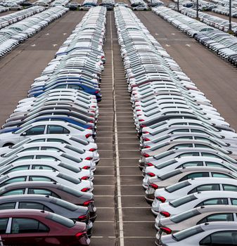 Rows of a new cars parked in a distribution center of a car factory. Top view to the parking in the open air.