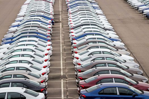 Rows of a new cars parked in a distribution center on a car factory on a cloudy day. Top view to the parking in the open air.