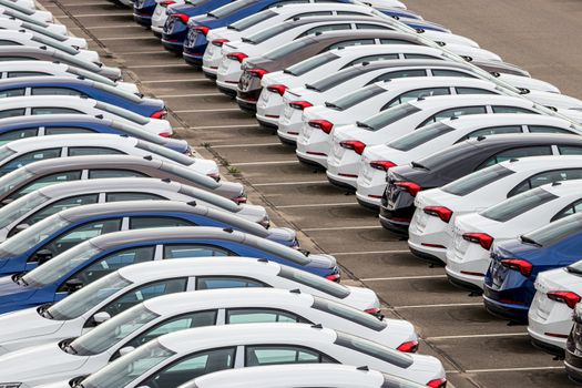 Rows of a new cars parked in a distribution center on a cloudy day in the spring, a car factory. Top view to the parking in the open air.