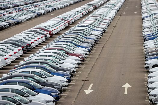 Rows of a new cars parked in a distribution center on a cloudy day in the spring, a car factory. Top view to the parking in the open air.