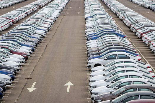 Rows of a new cars parked in a distribution center on a car factory on a cloudy day. Top view to the parking in the open air.