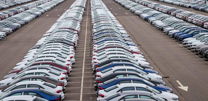 Rows of a new cars parked in a distribution center on a cloudy day in the spring, a car factory. Top view to the parking in the open air.