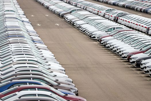 Rows of a new cars parked in a distribution center on a cloudy day in the spring, a car factory. Top view to the parking in the open air.