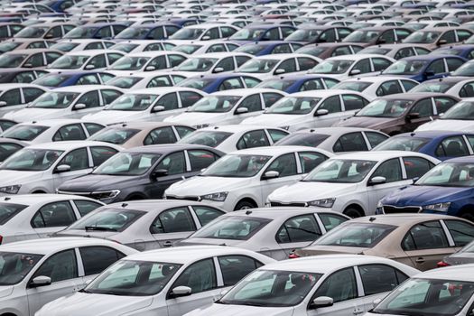 Rows of a new cars parked in a distribution center of a car factory. Top view to the parking in the open air.