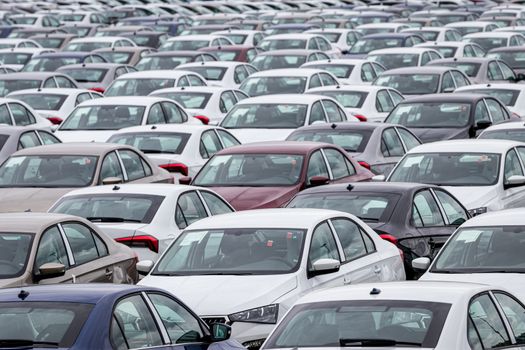 Rows of a new cars parked in a distribution center on a cloudy day in the spring, a car factory. Top view to the parking in the open air.