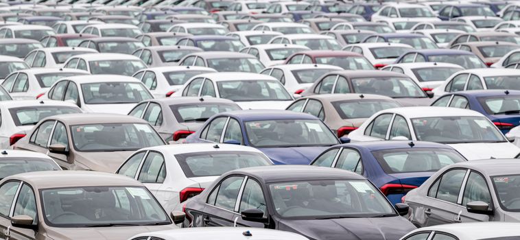 Rows of a new cars parked in a distribution center of a car factory. Top view to the parking in the open air.