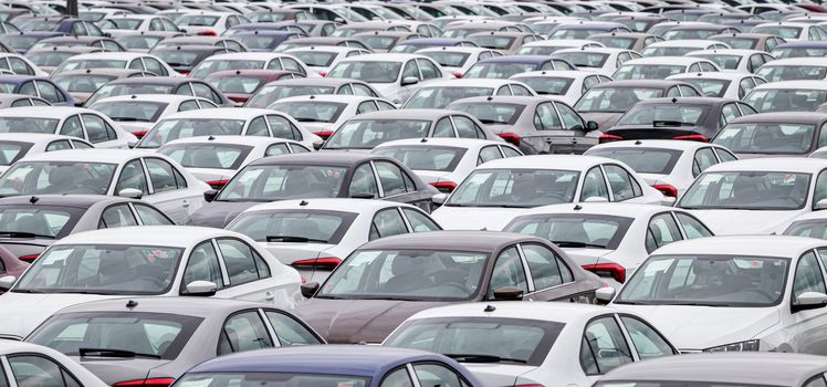 Rows of a new cars parked in a distribution center on a cloudy day in the spring, a car factory. Top view to the parking in the open air.