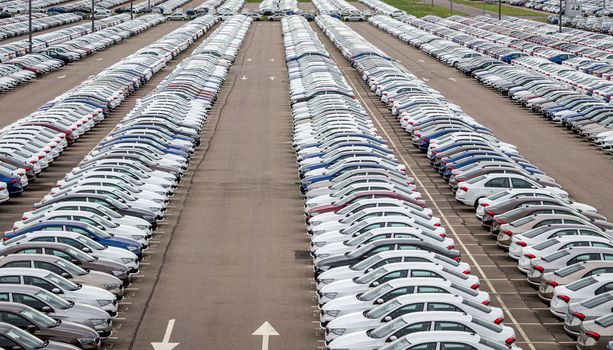 Rows of a new cars parked in a distribution center on a cloudy day in the spring, a car factory. Top view to the parking in the open air.