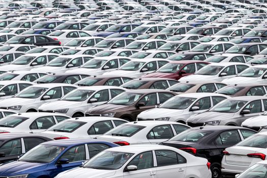 Rows of a new cars parked in a distribution center on a cloudy day in the spring, a car factory. Top view to the parking in the open air.