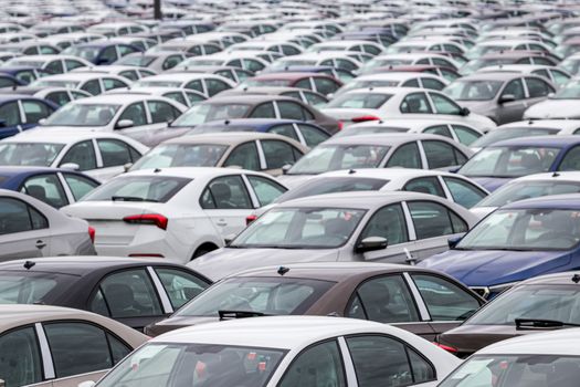 Rows of a new cars parked in a distribution center on a cloudy day in the spring, a car factory. Top view to the parking in the open air.