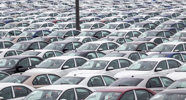 Rows of a new cars parked in a distribution center on a cloudy day in the spring, a car factory. Top view to the parking in the open air.