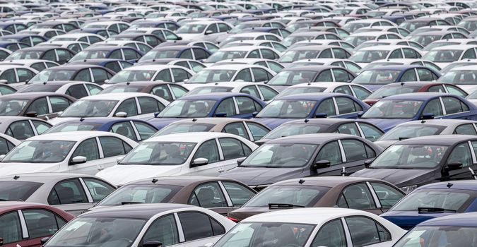 Rows of a new cars parked in a distribution center of a car factory. Top view to the parking in the open air.