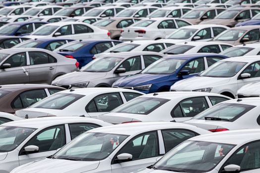 Rows of a new cars parked in a distribution center on a cloudy day in the spring, a car factory. Top view to the parking in the open air.