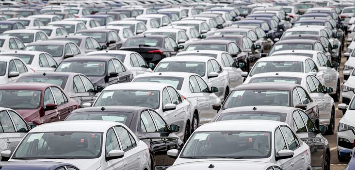 Rows of a new cars parked in a distribution center on a cloudy day in the spring, a car factory. Top view to the parking in the open air.