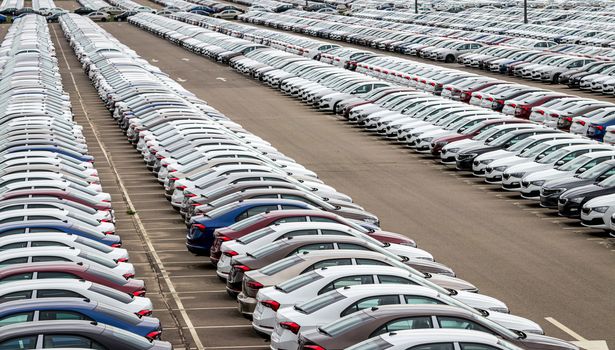 Rows of a new cars parked in a distribution center on a cloudy day in the spring, a car factory. Top view to the parking in the open air.