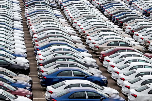 Rows of a new cars parked in a distribution center of a car factory. Top view to the parking in the open air.