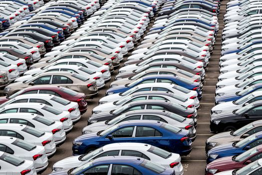 Rows of a new cars parked in a distribution center on a cloudy day in the spring, a car factory. Top view to the parking in the open air.