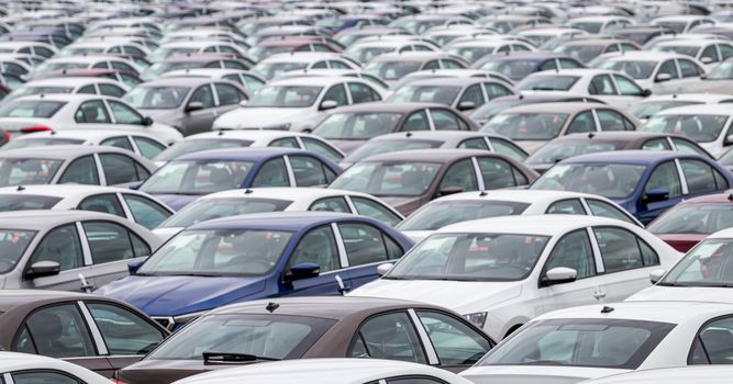 Rows of a new cars parked in a distribution center of a car factory. Top view to the parking in the open air.