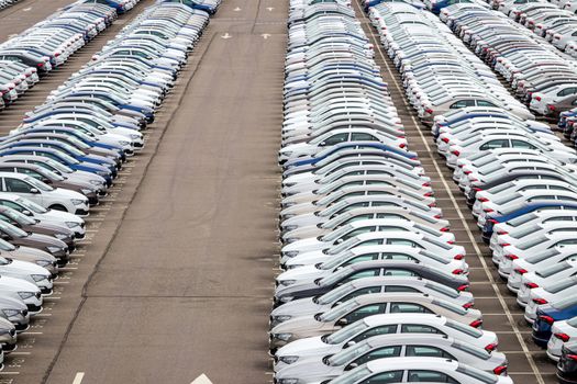 Rows of a new cars parked in a distribution center on a car factory on a cloudy day. Top view to the parking in the open air.