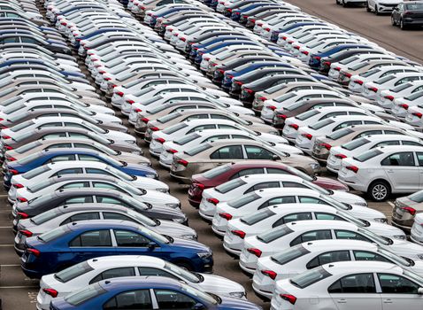 Rows of a new cars parked in a distribution center on a car factory on a cloudy day. Top view to the parking in the open air.