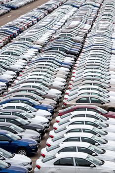 Rows of a new cars parked in a distribution center on a cloudy day in the spring, a car factory. Top view to the parking in the open air.