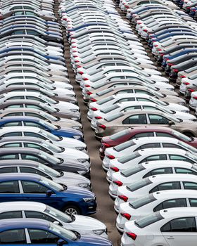 Rows of a new cars parked in a distribution center of a car factory. Top view to the parking in the open air.