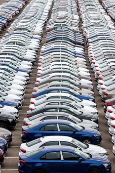 Rows of a new cars parked in a distribution center on a cloudy day in the spring, a car factory. Top view to the parking in the open air.