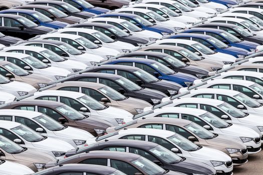 Rows of a new cars parked in a distribution center on a car factory on a cloudy day. Top view to the parking in the open air.