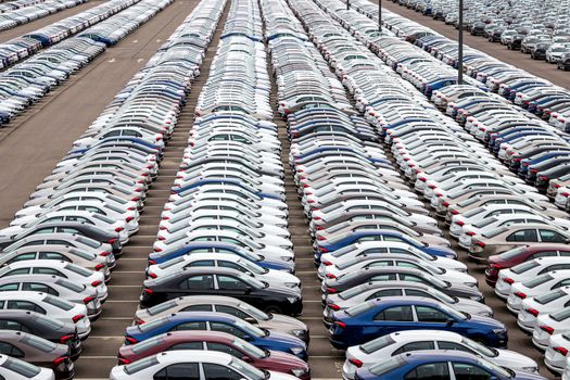 Rows of a new cars parked in a distribution center of a car factory. Top view to the parking in the open air.