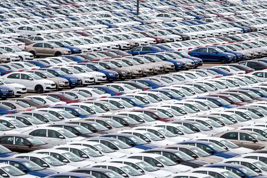 Rows of a new cars parked in a distribution center on a cloudy day in the spring, a car factory. Top view to the parking in the open air.