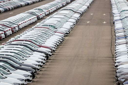 Rows of a new cars parked in a distribution center of a car factory. Top view to the parking in the open air.