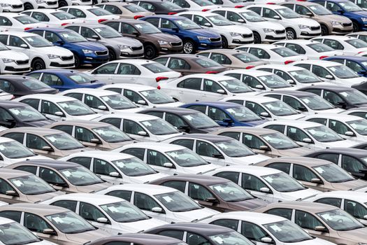 Rows of a new cars parked in a distribution center of a car factory. Top view to the parking in the open air.