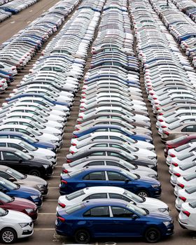 Rows of a new cars parked in a distribution center on a cloudy day in the spring, a car factory. Top view to the parking in the open air.