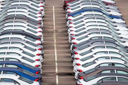 Rows of a new cars parked in a distribution center on a car factory on a cloudy day. Top view to the parking in the open air.