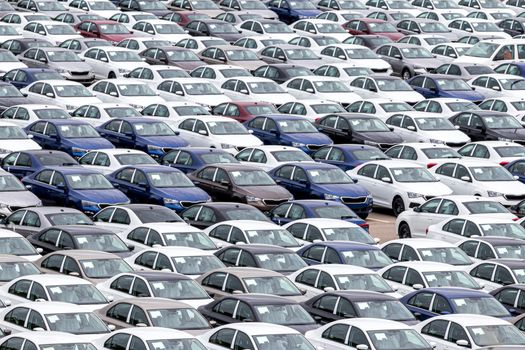 Rows of a new cars parked in a distribution center of a car factory. Top view to the parking in the open air.