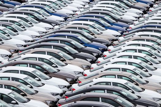 Rows of a new cars parked in a distribution center on a cloudy day in the spring, a car factory. Top view to the parking in the open air.