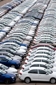 Rows of a new cars parked in a distribution center of a car factory. Top view to the parking in the open air.