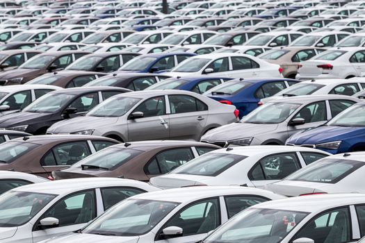 Rows of a new cars parked in a distribution center on a car factory on a cloudy day. Top view to the parking in the open air.