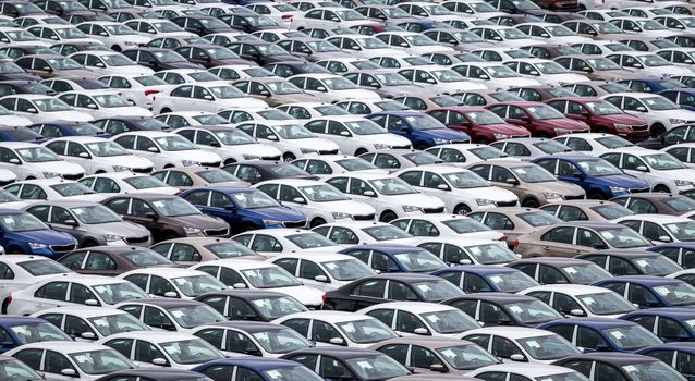 Rows of a new cars parked in a distribution center on a cloudy day in the spring, a car factory. Top view to the parking in the open air.