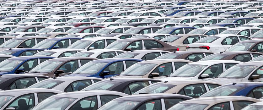 Rows of a new cars parked in a distribution center on a car factory on a cloudy day. Top view to the parking in the open air.