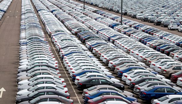 Rows of a new cars parked in a distribution center on a cloudy day in the spring, a car factory. Top view to the parking in the open air.