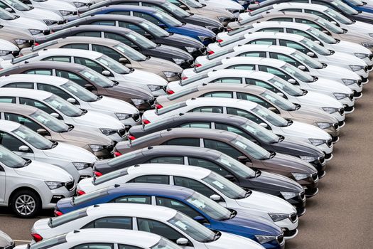 Rows of a new cars parked in a distribution center on a car factory on a cloudy day. Top view to the parking in the open air.