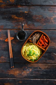 Homemade Bento pack lunch, grilled beef and noodles with ingredients top view dark wooden table