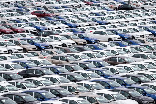 Rows of a new cars parked in a distribution center on a car factory on a cloudy day. Top view to the parking in the open air.