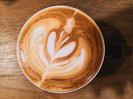 Hot latte coffee with a heart shaped milk sponge on a wooden table