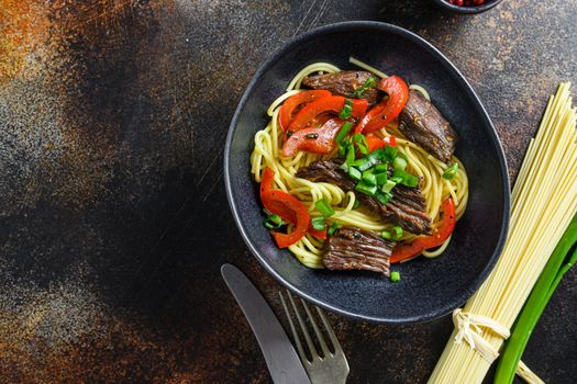 Chinese noodles with vegetables and beef in black bowl top view close up space for text..