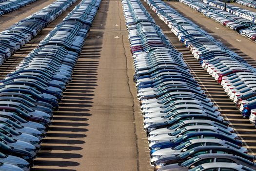 Rows of a new cars parked in a distribution center on a car factory on a sunny day. Top view to the parking in the open air.