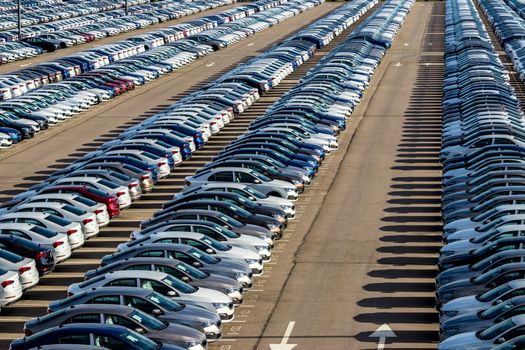 Rows of a new cars parked in a distribution center on a car factory on a sunny day. Top view to the parking in the open air.