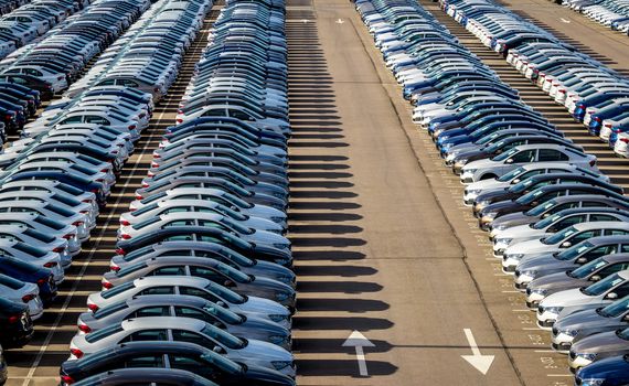 Rows of a new cars parked in a distribution center on a car factory on a sunny day. Top view to the parking in the open air.