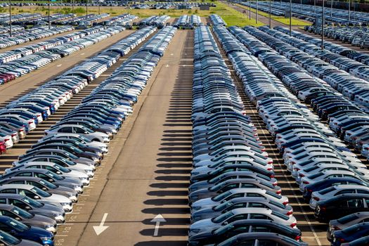 Rows of a new cars parked in a distribution center on a car factory on a sunny day. Parking in the open air.